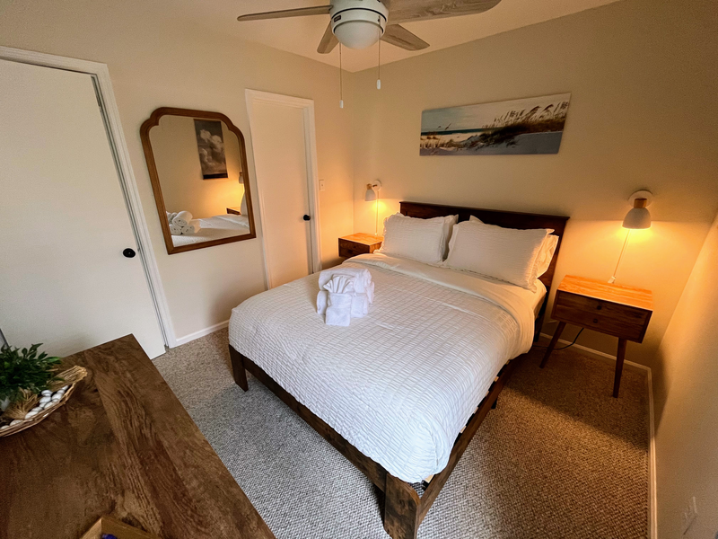 Cozy queen bedroom with warm lighting, ceiling fan, and coastal style