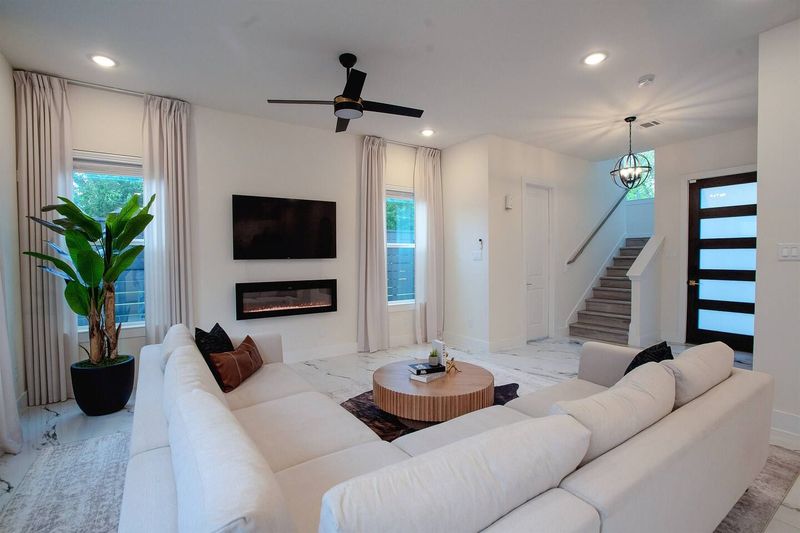 Spacious living room with a plush sectional, smart TV with Apple AirPlay, color-changing electric fireplace, and marble floors. Bright natural light and an open layout create a clean, modern space to relax.