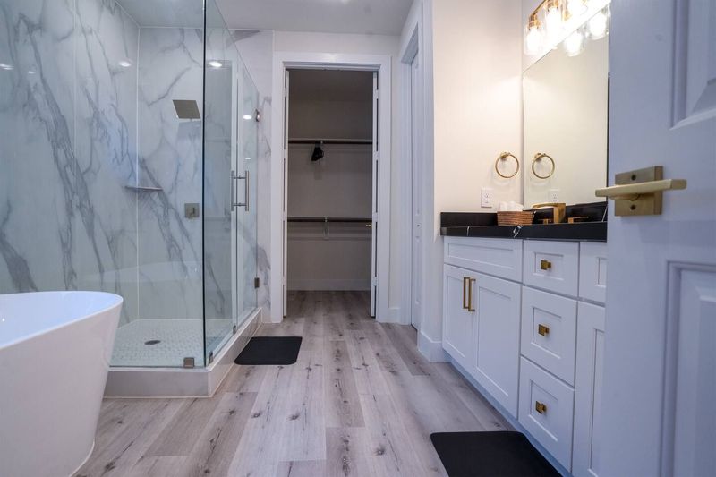Spa-style bathroom with a soaking tub, walk-in glass shower, separate enclosed restroom, walk-in closet, and built-in shampoo, conditioner, and body wash dispensers.
