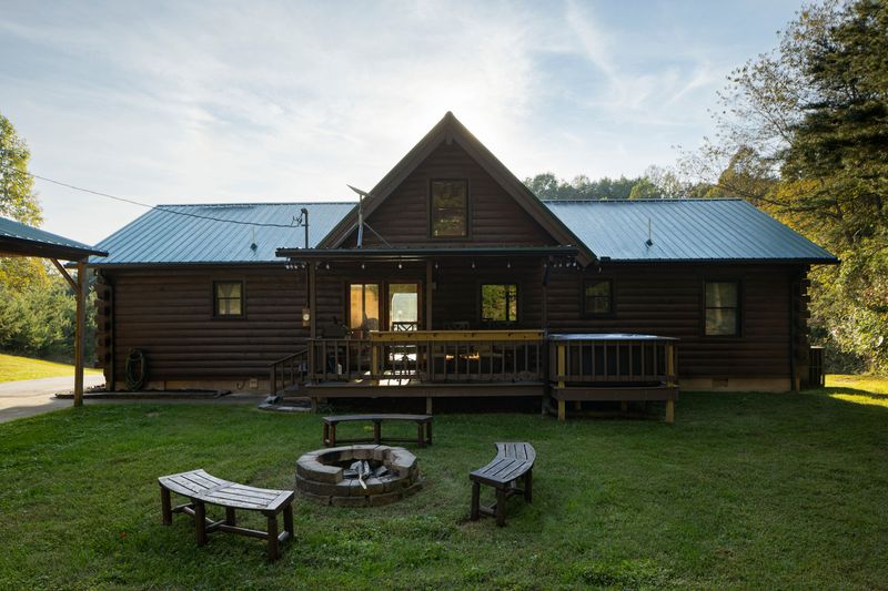 Rustic log cabin with porch, deck, and fire pit in a peaceful wooded setting
